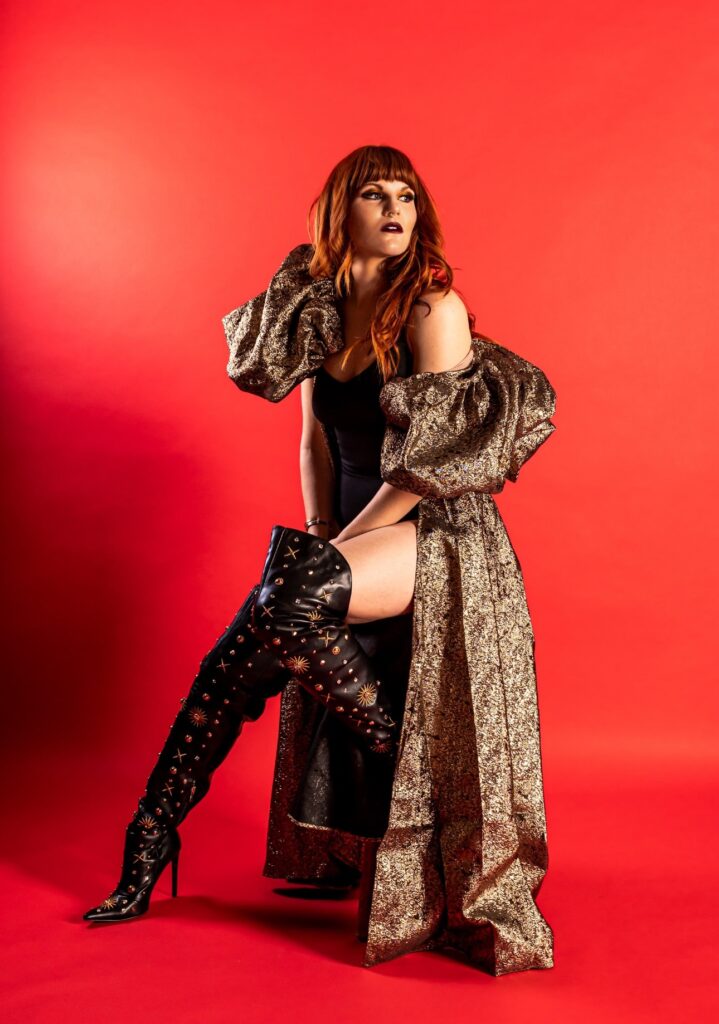Monte in standing pose with a long jacket and knee high boots.