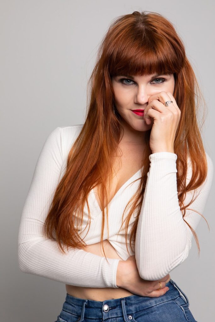Monte in a casual pose with her hand near her face, in a white top.