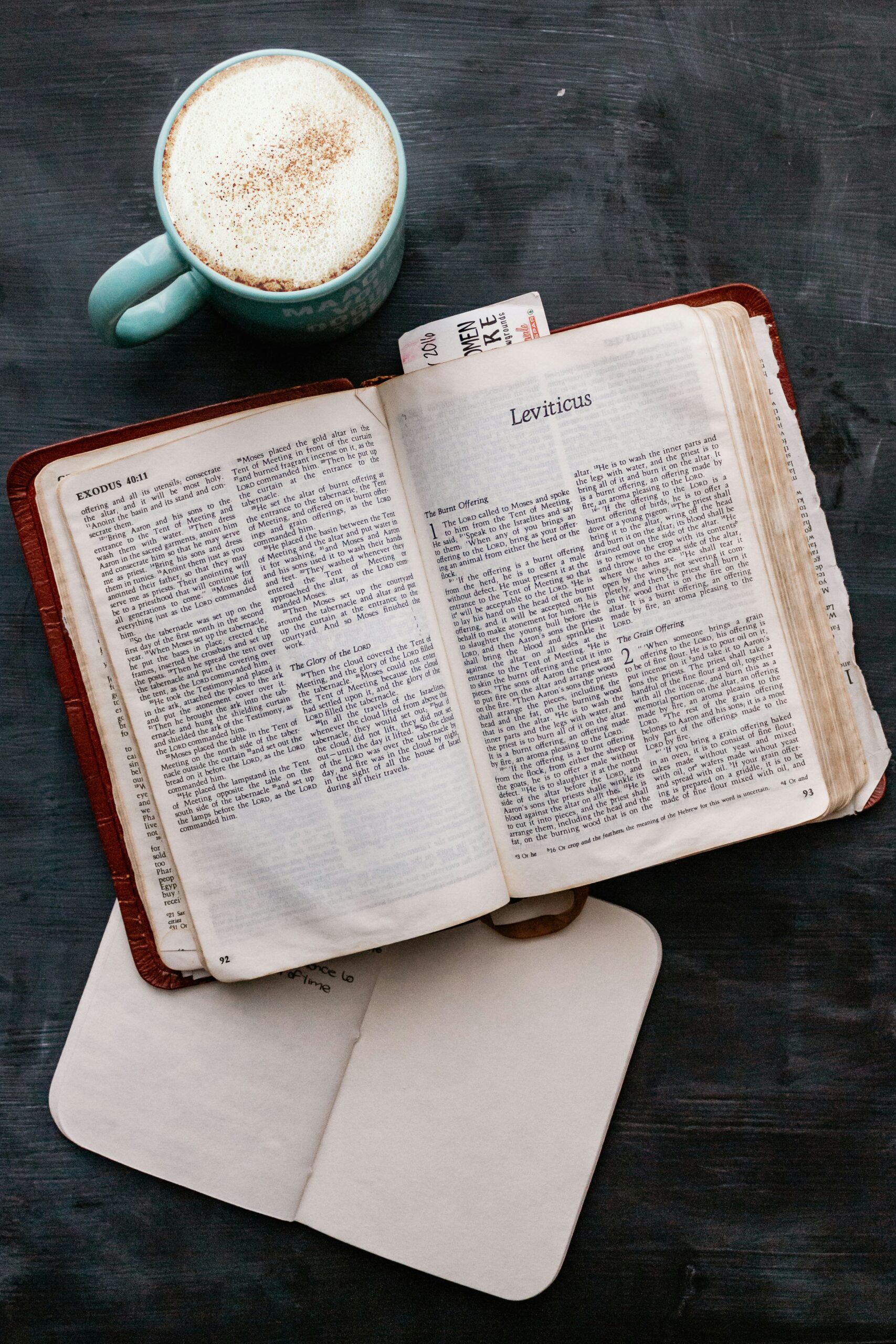 Bible, notebook, and a hot beverage in a mug on a table.